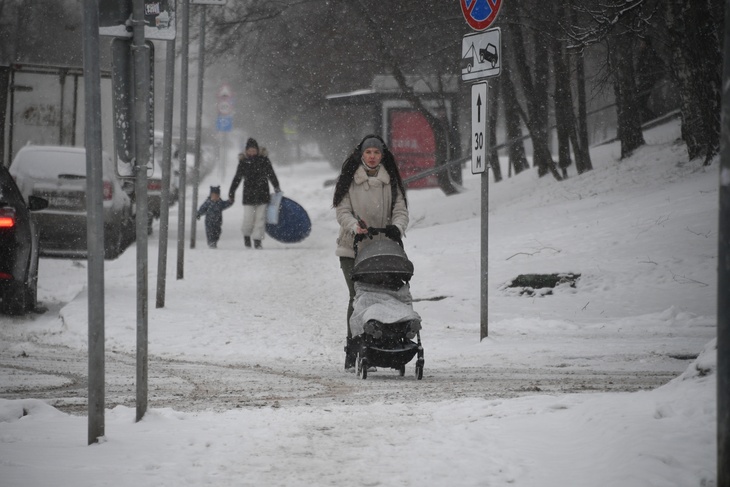 Женщина с детской коляской на прогулке во время снегопада.